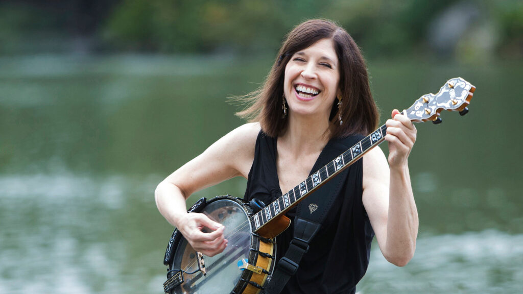 Cynthia Sayer with banjo in front of a lake