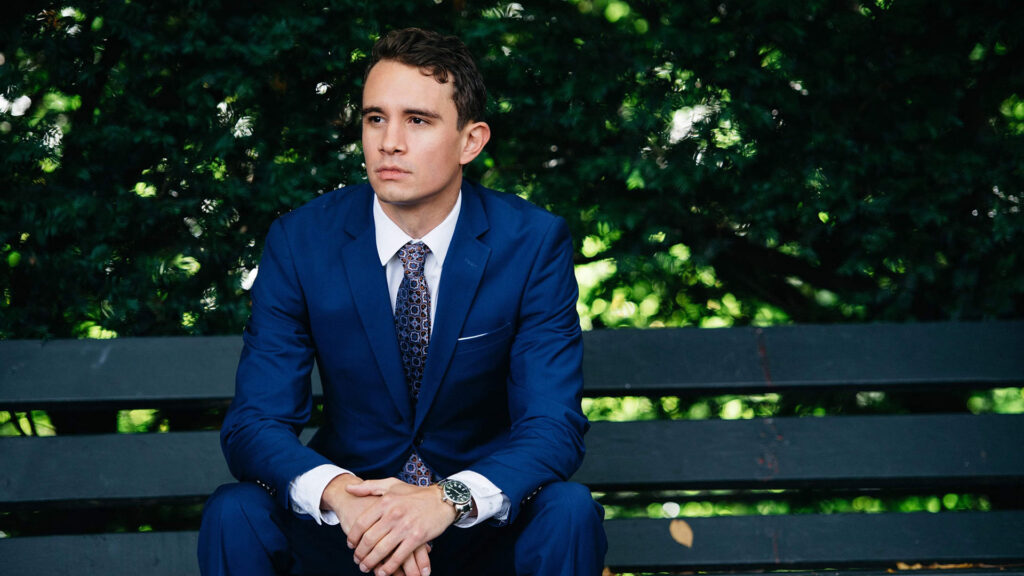 Michael Noble in blue suit sitting on a bench