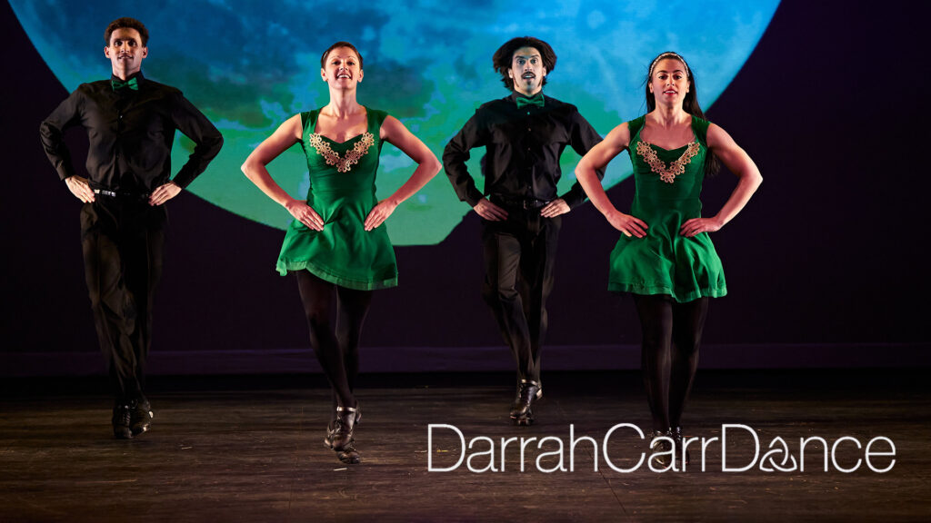 Four dancers in green and black costumes perform on stage with a celestial backdrop. Text reads "Darrah Carr Dance."