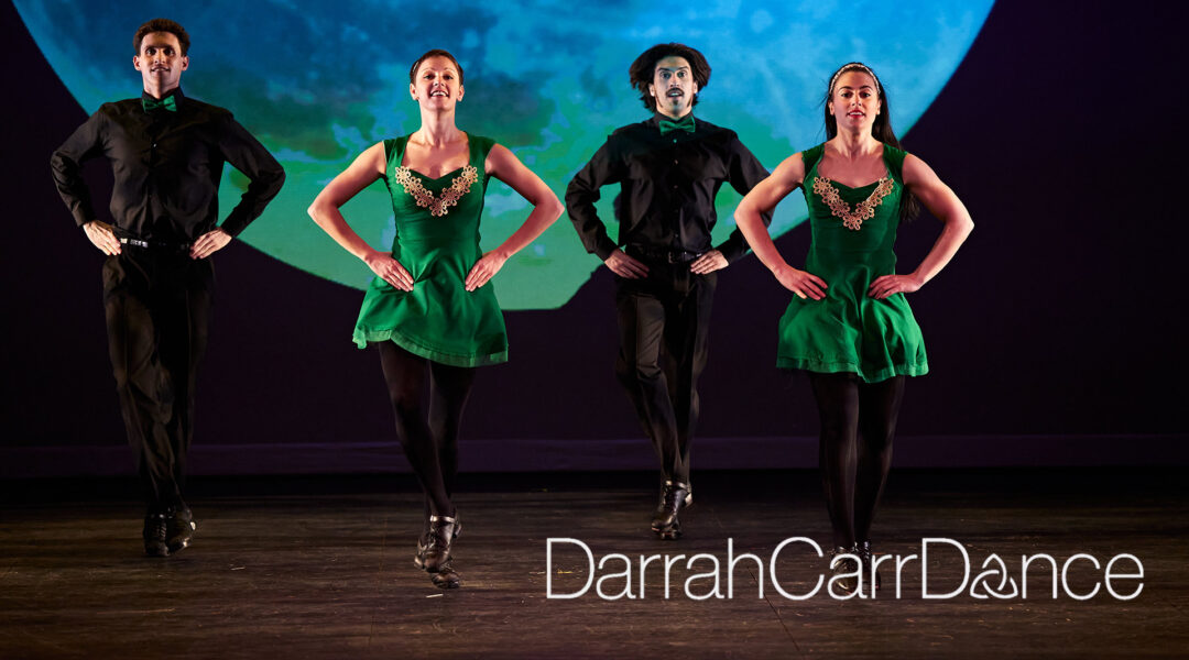 Four dancers in green and black costumes perform on stage with a celestial backdrop. Text reads "Darrah Carr Dance."