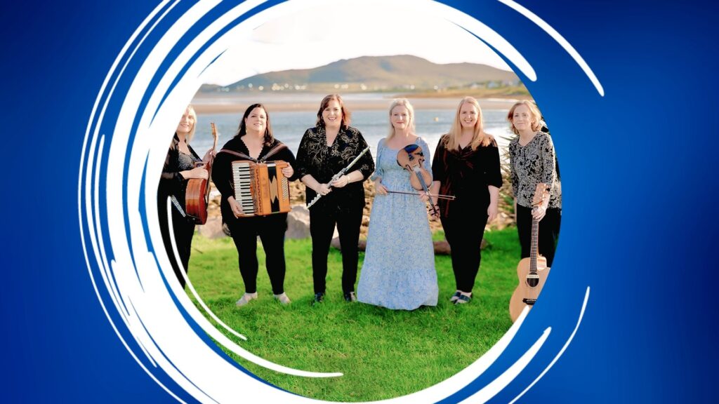 Six women with musical instruments standing on a grassy area by water.