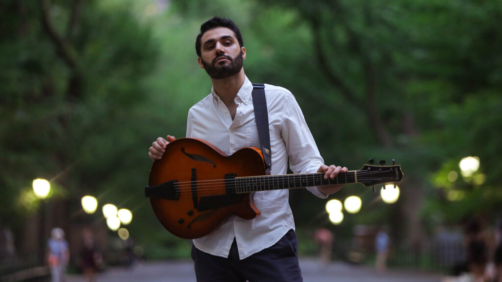 Person in a park holding a semi-hollow electric guitar.