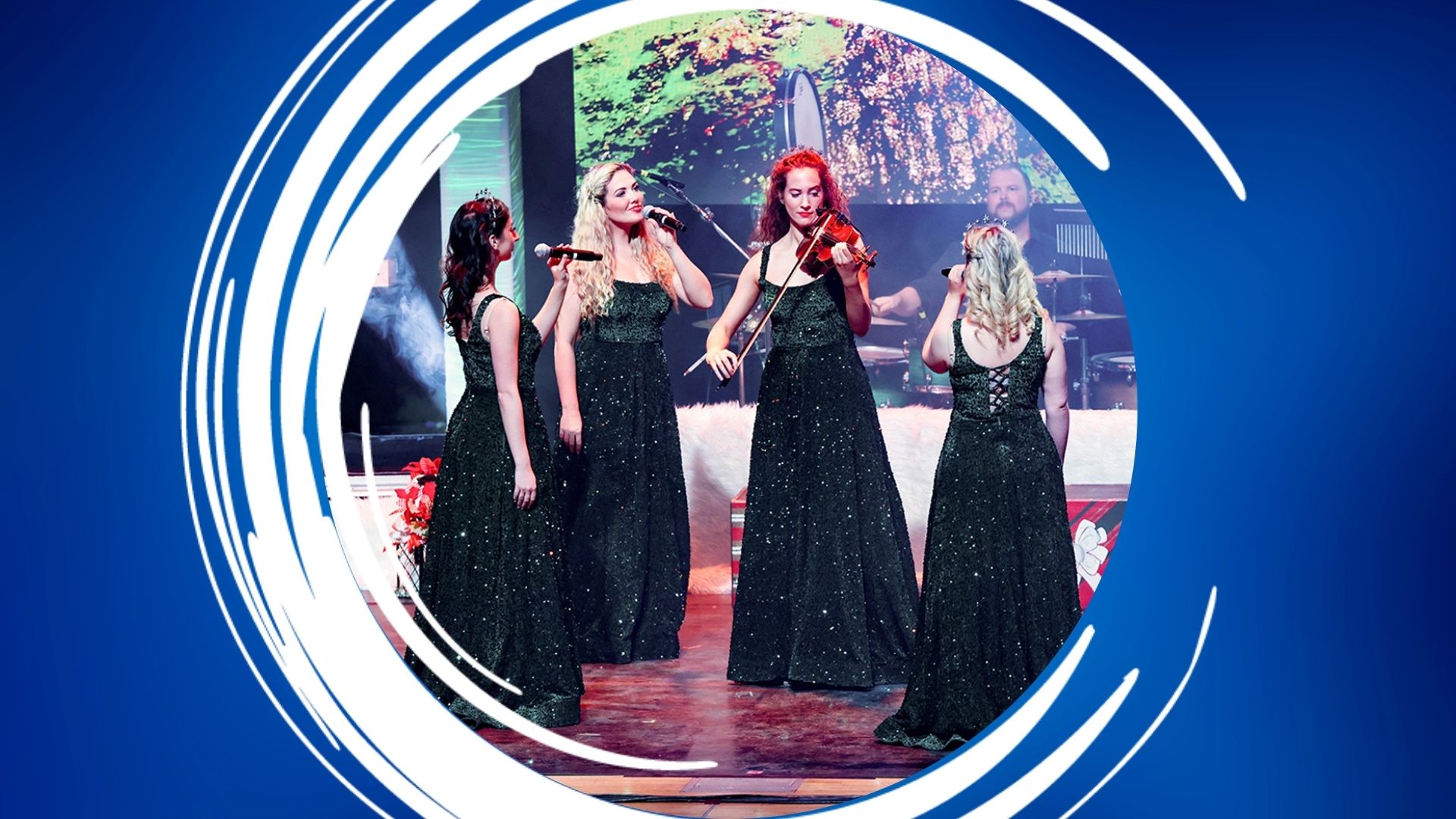 Four women in sparkly black gowns performing on stage, one playing a violin and the others singing, with a drummer in the background.