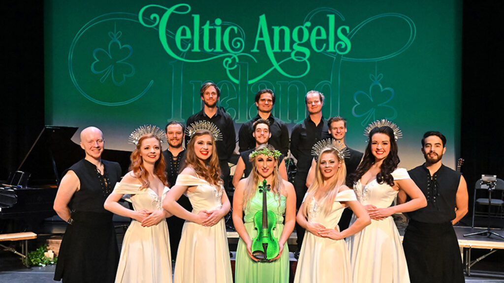 Performers on stage with "Celtic Angels Ireland" backdrop, women in white dresses and men in black attire.
