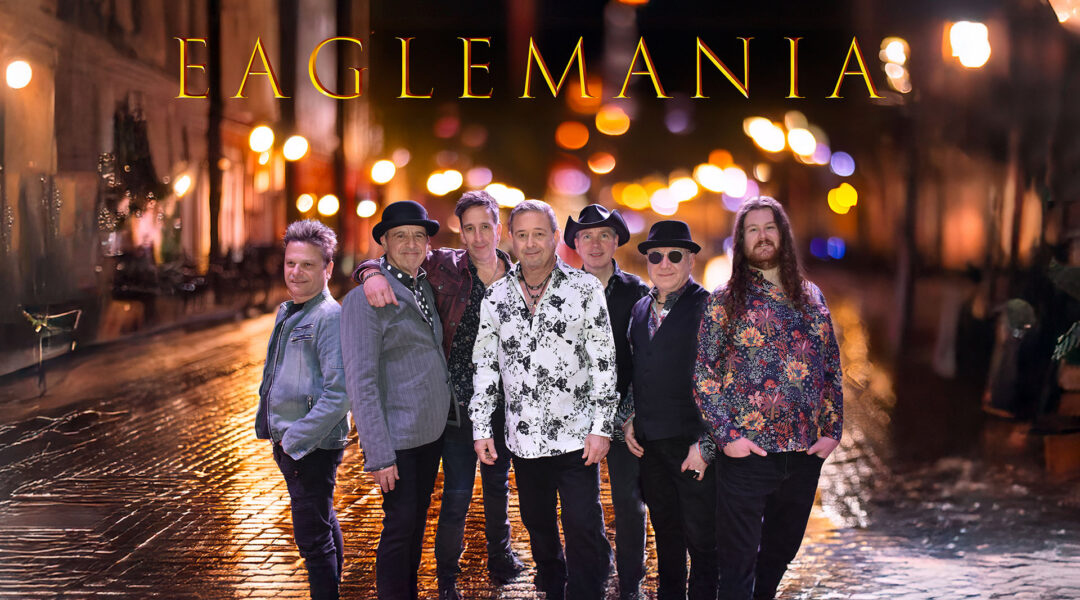A group of seven men in varied attire standing on a dimly lit cobblestone street at night with blurred streetlights in the background.
