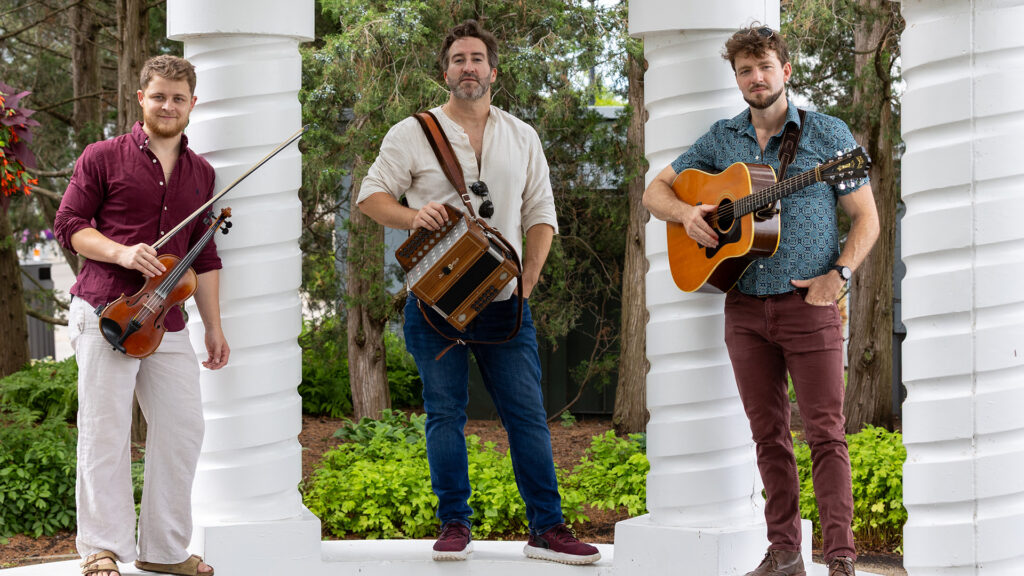 Three men with musical instruments standing between white columns surrounded by greenery.