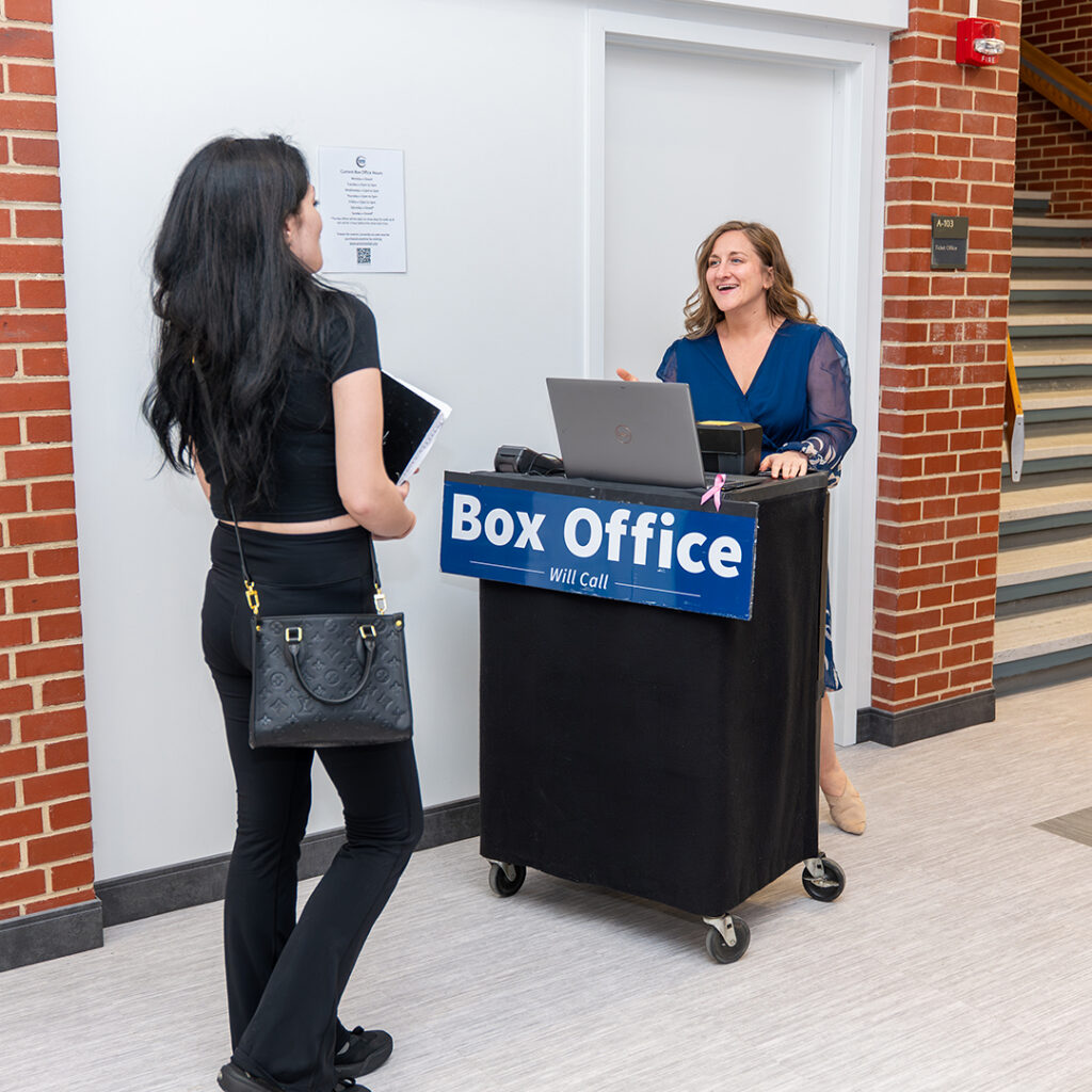 A woman at a box office cart interacts with a visitor buying tickets at the Grunin Center.
