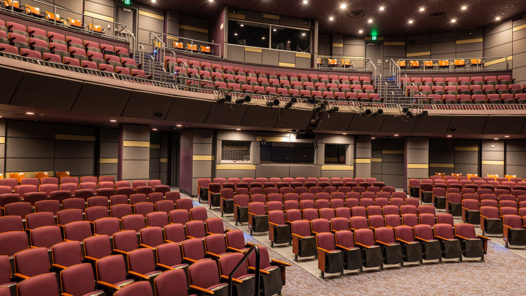 A large auditorium with red seats, balcony seating, and stage lights.