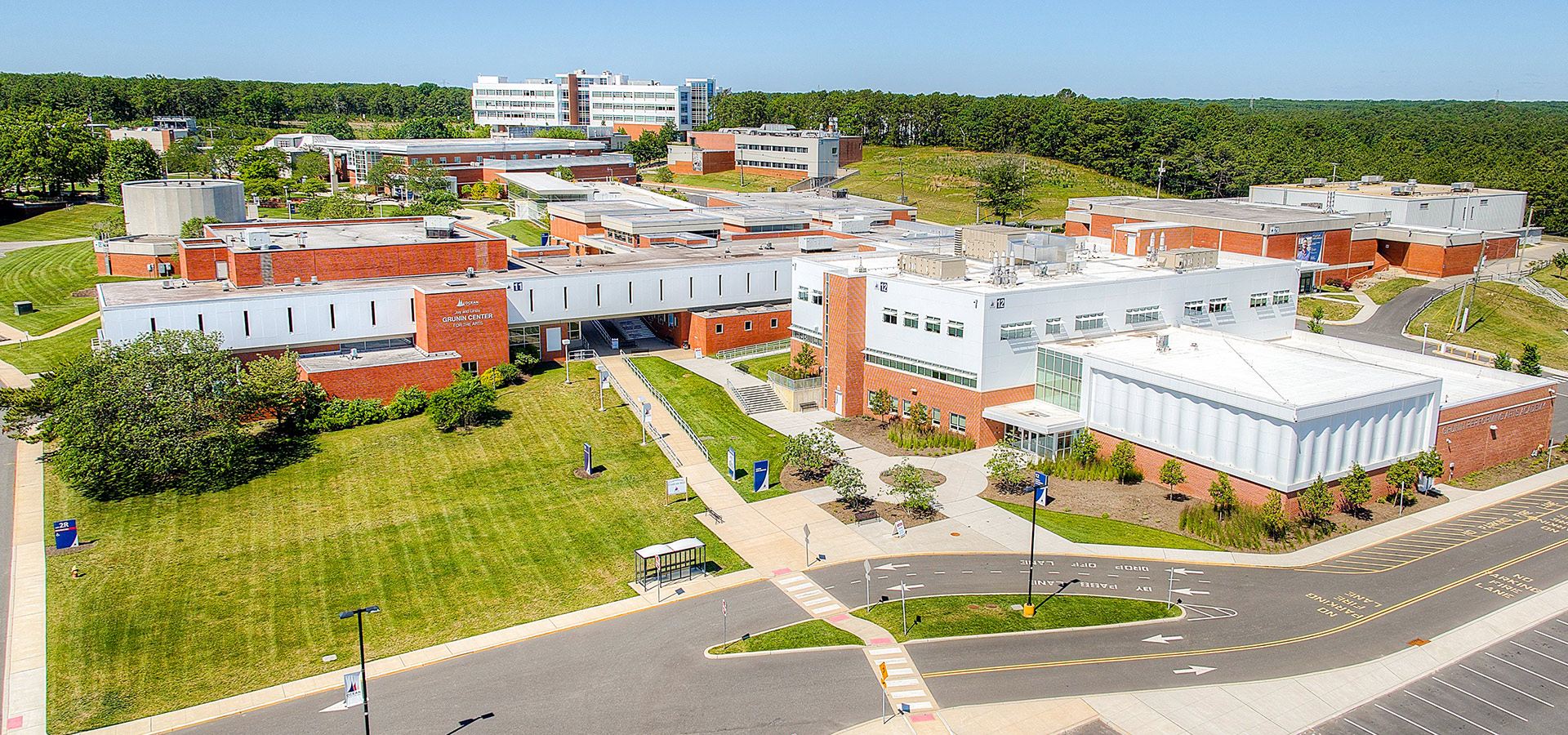 Aerial view of a university campus with interconnected buildings, green lawns, and a backdrop of trees.