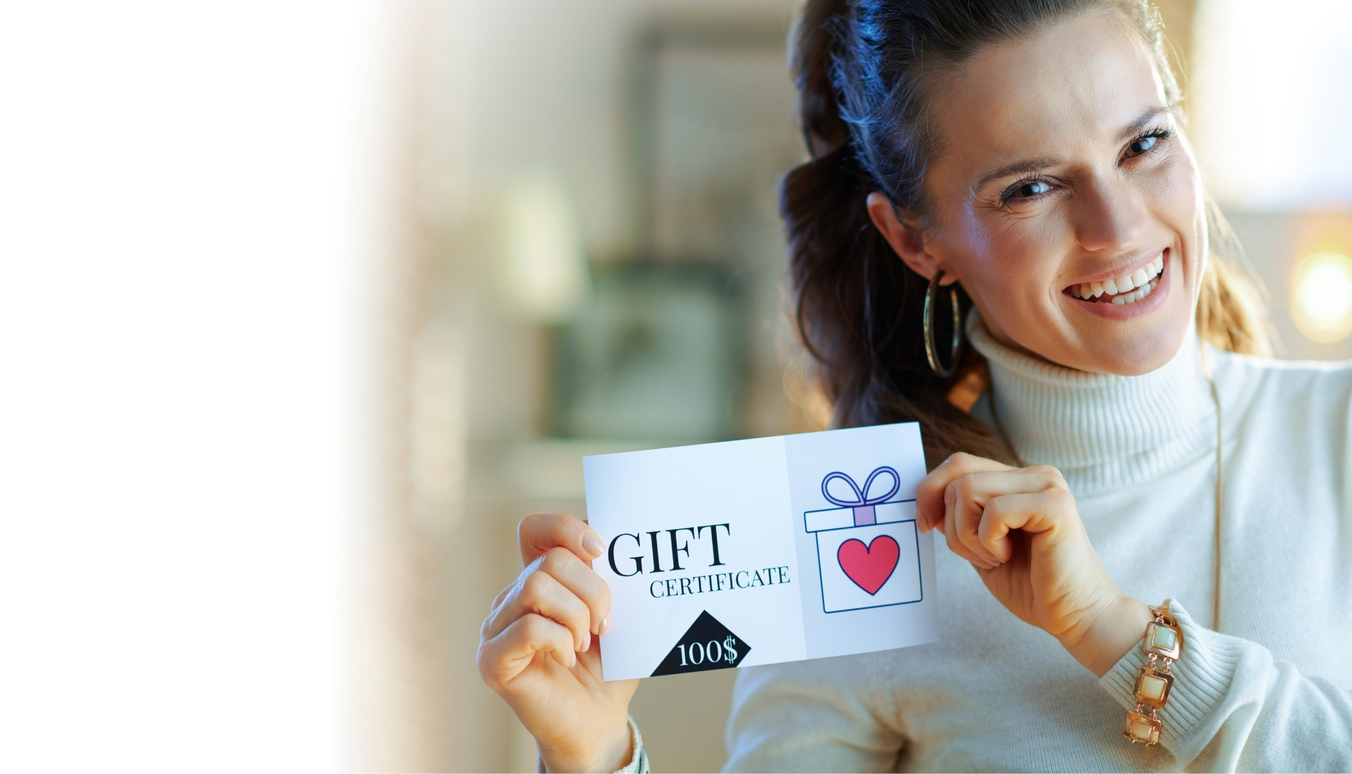 A person smiling while holding a gift certificate with a gift box illustration and the text "GIFT CERTIFICATE 100$".