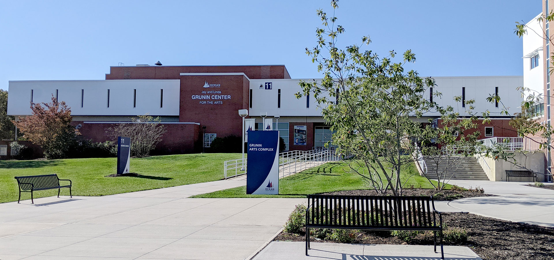 The exterior of the Jay and Linda Grunin Center for the Arts, featuring a red brick and white facade with surrounding greenery.