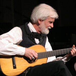 An older man with white hair playing a classical guitar on stage.