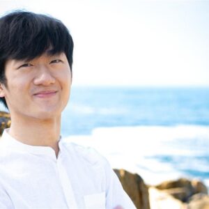 Person smiling near a rocky coastal area with the sea in the background.