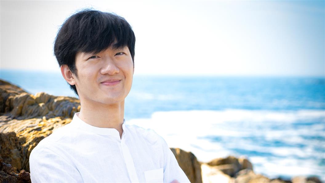 Person smiling near a rocky coastal area with the sea in the background.