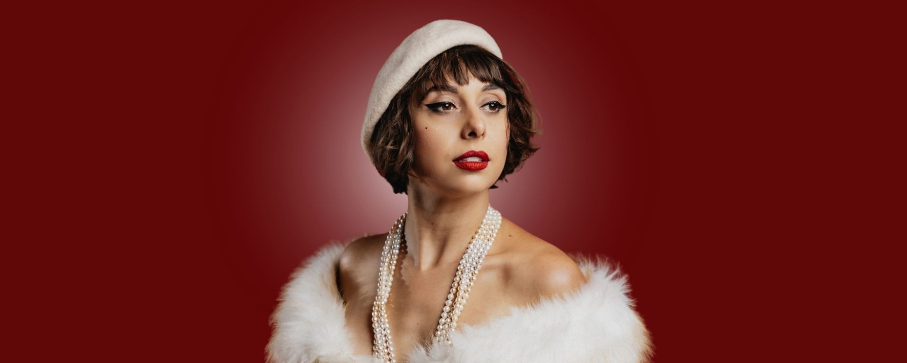 Person in a white beret and fluffy white garment against a red background.