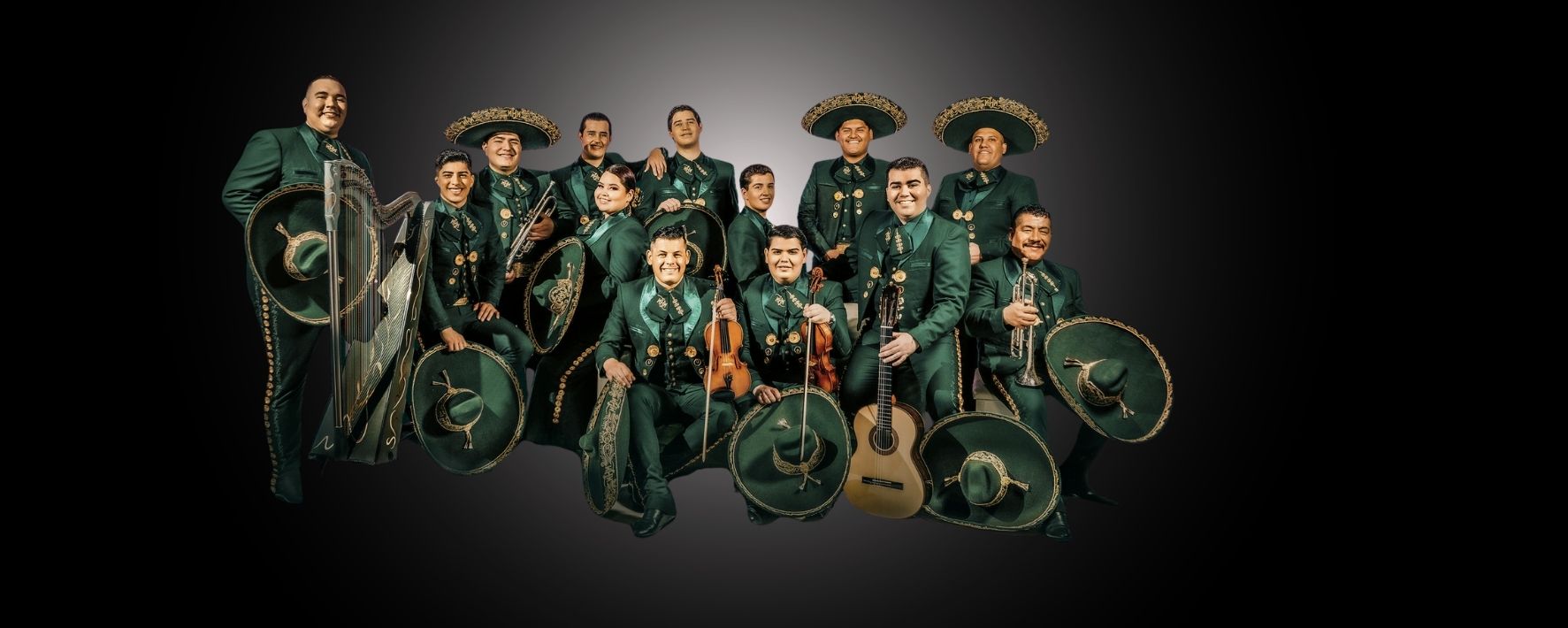 A mariachi band of thirteen members in green charro suits with gold embroidery, holding instruments including guitars, violins, a trumpet, and a harp.
