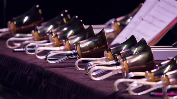 Row of polished handbells with white handles on a dark surface, sheet music in the background.