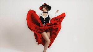 Person in a red skirt and black vest posing dynamically, with a black and red hat.
