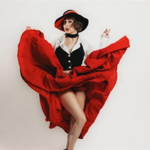 Person in a red skirt and black vest posing dynamically, with a black and red hat.